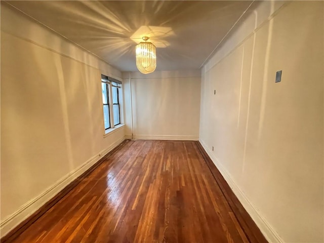 spare room featuring dark wood-type flooring and a chandelier