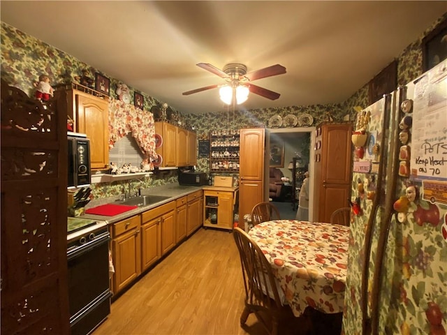 kitchen with light countertops, light wood-style flooring, stove, a sink, and wallpapered walls