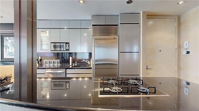 kitchen with built in appliances, sink, white cabinets, and dark stone countertops