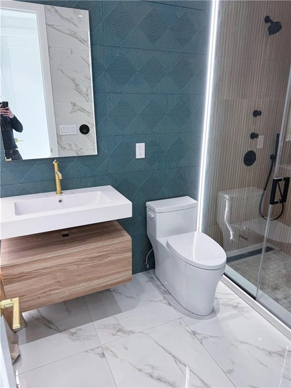 bathroom with vanity, toilet, a shower with shower door, and tile walls