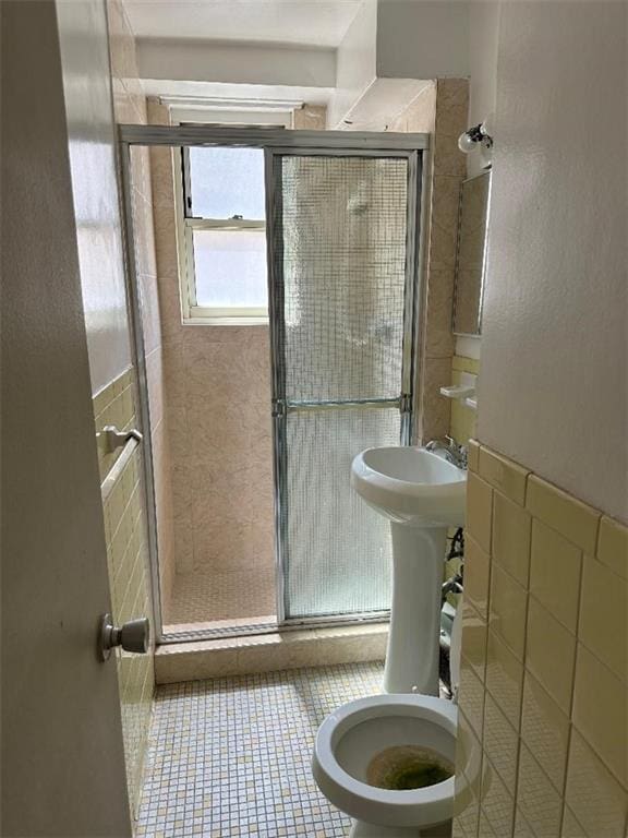 bathroom with a shower with door, sink, tile walls, tile patterned floors, and toilet