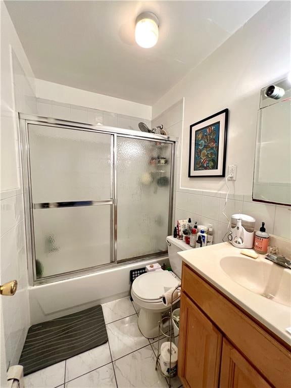 full bathroom featuring tile walls, enclosed tub / shower combo, toilet, tile flooring, and vanity