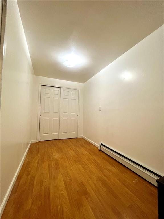 unfurnished bedroom featuring wood-type flooring and a baseboard heating unit