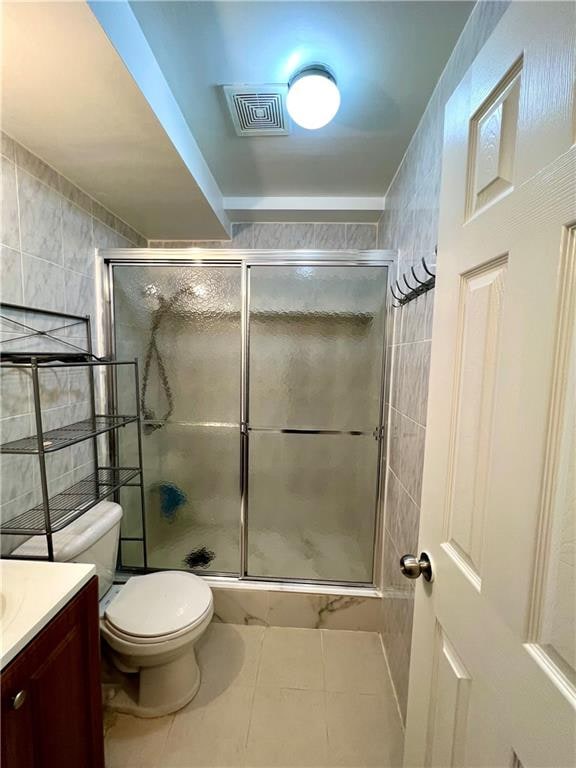 bathroom featuring tile flooring, tile walls, a shower with door, vanity, and toilet