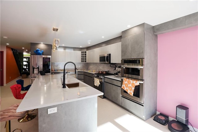 kitchen with a large island, modern cabinets, a sink, backsplash, and appliances with stainless steel finishes