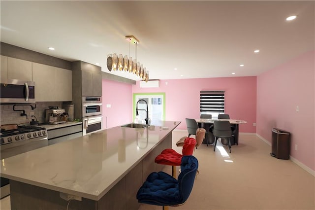 kitchen with a center island with sink, recessed lighting, a sink, appliances with stainless steel finishes, and backsplash