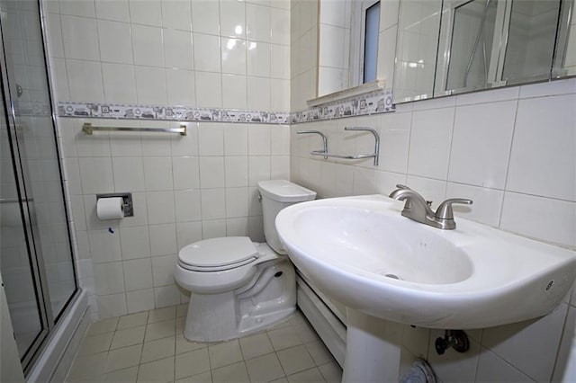 bathroom with toilet, sink, tile walls, a shower with door, and tile patterned flooring