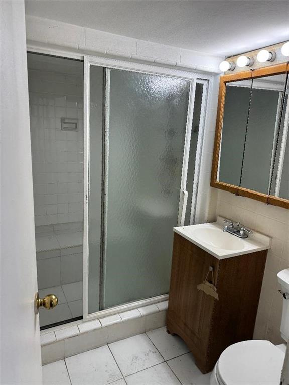 bathroom featuring tile patterned flooring, walk in shower, vanity, and toilet