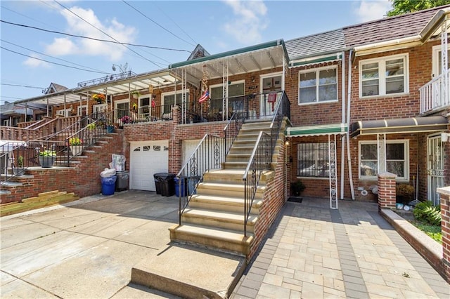 view of property with driveway, roof with shingles, an attached garage, brick siding, and stairs