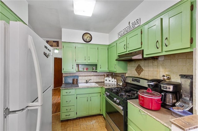 kitchen with decorative backsplash, under cabinet range hood, stainless steel range with gas stovetop, and freestanding refrigerator