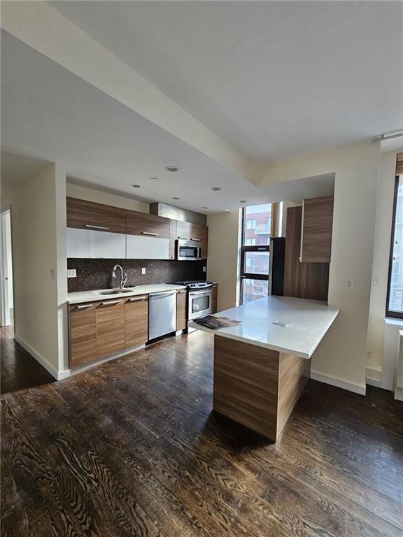 kitchen featuring modern cabinets, a sink, appliances with stainless steel finishes, decorative backsplash, and dark wood-style flooring