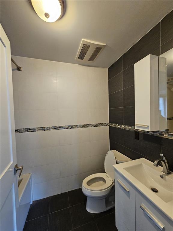 bathroom with visible vents, toilet, tile walls, tile patterned flooring, and vanity