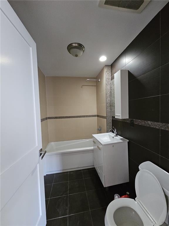 bathroom featuring visible vents, toilet, bathing tub / shower combination, tile patterned floors, and tile walls