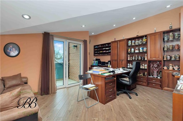 office space with vaulted ceiling, built in desk, and light hardwood / wood-style flooring