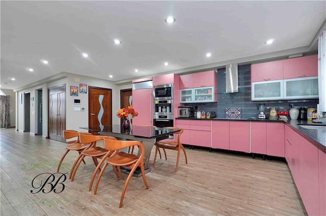 kitchen with built in appliances, wall chimney exhaust hood, light hardwood / wood-style floors, and decorative backsplash