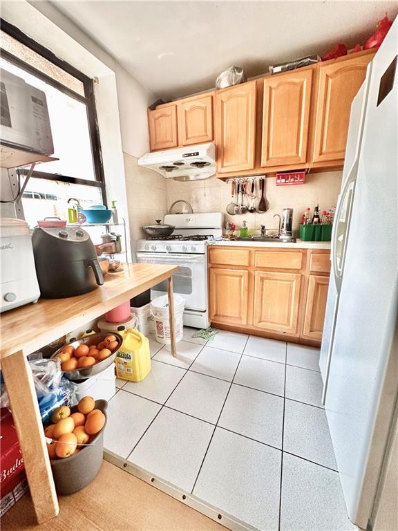 kitchen featuring white appliances, light brown cabinetry, and exhaust hood