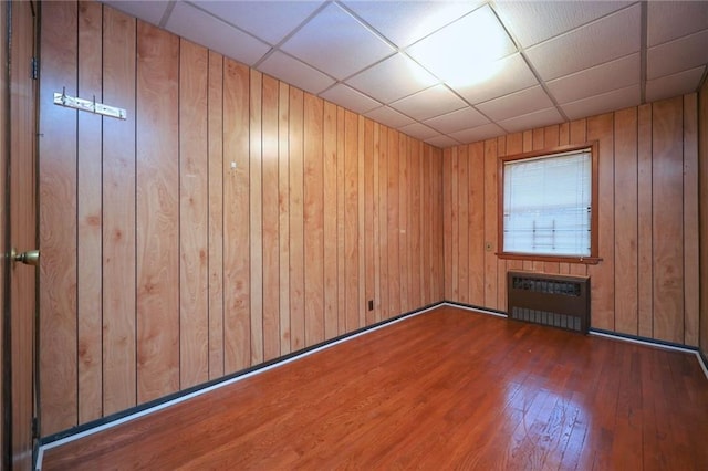 empty room featuring wood walls, radiator heating unit, dark hardwood / wood-style floors, and a paneled ceiling