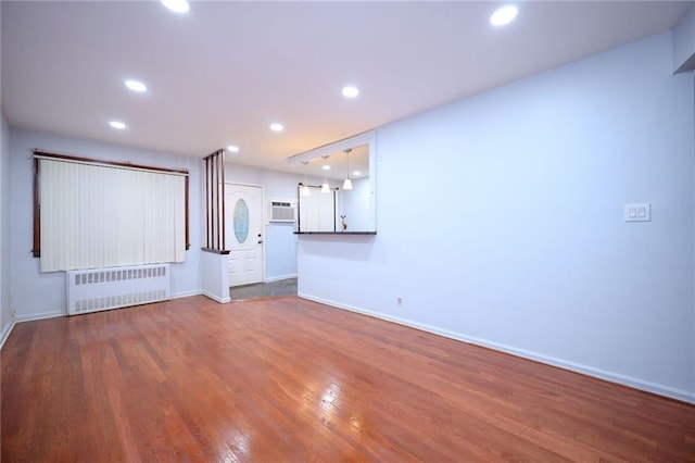 unfurnished living room featuring wood-type flooring, an AC wall unit, and radiator