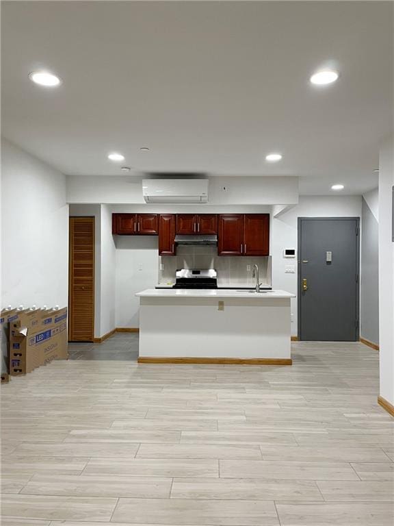 kitchen with a center island with sink, a wall mounted air conditioner, stove, backsplash, and sink