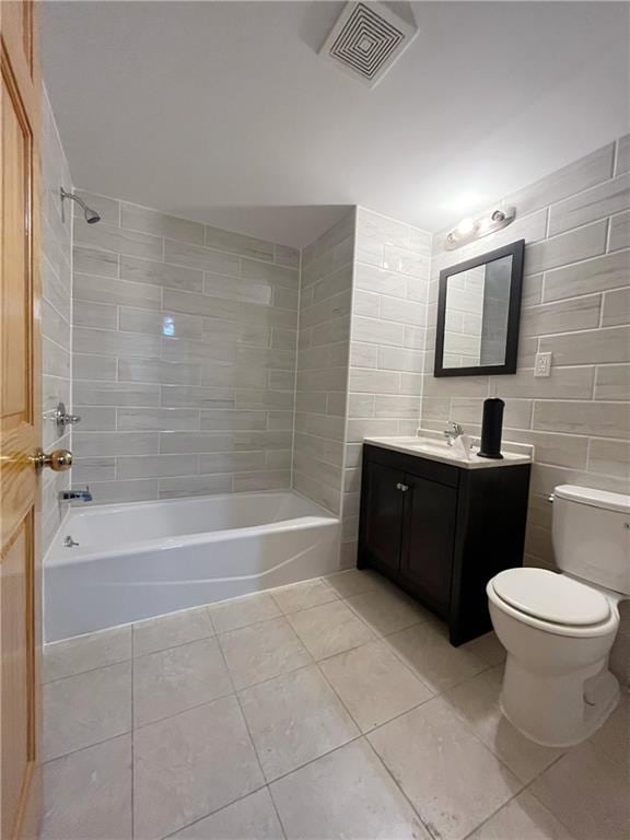 full bathroom featuring toilet, tile walls, vanity, tiled shower / bath combo, and tile patterned flooring