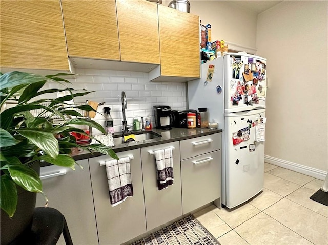 kitchen with a sink, backsplash, dark countertops, freestanding refrigerator, and light tile patterned flooring