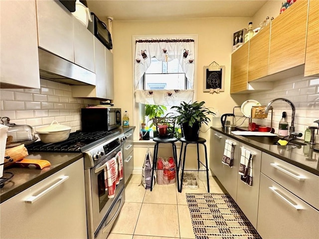 kitchen with a sink, under cabinet range hood, dark countertops, stainless steel appliances, and light tile patterned floors