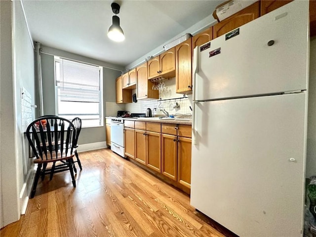 kitchen featuring baseboards, light countertops, decorative backsplash, freestanding refrigerator, and light wood-style floors