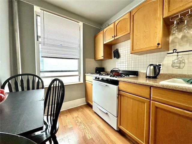 kitchen with white range with gas stovetop, baseboards, tasteful backsplash, and light wood finished floors