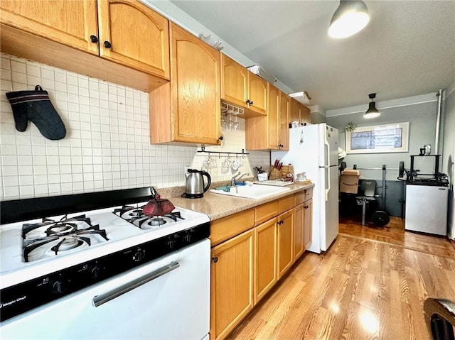 kitchen with a sink, backsplash, white appliances, light wood-style floors, and light countertops