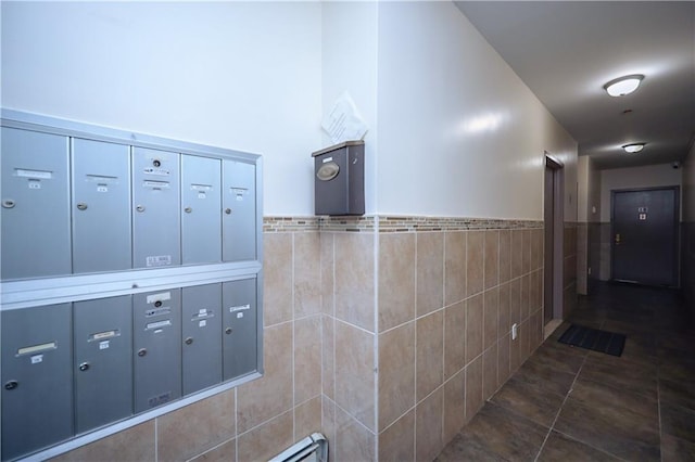 corridor featuring mail boxes, dark tile patterned floors, and tile walls