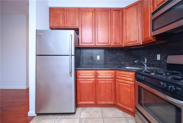 kitchen with sink, stainless steel appliances, backsplash, dark stone counters, and light tile patterned floors