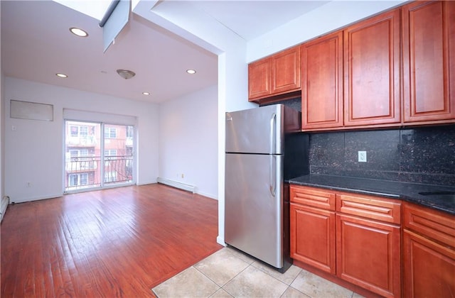 kitchen with tasteful backsplash, a baseboard radiator, dark stone countertops, stainless steel refrigerator, and light tile patterned flooring