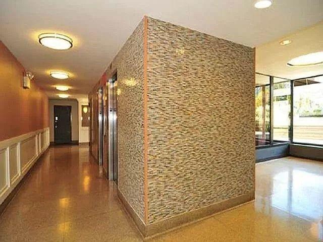 hall featuring a decorative wall, granite finish floor, and wainscoting