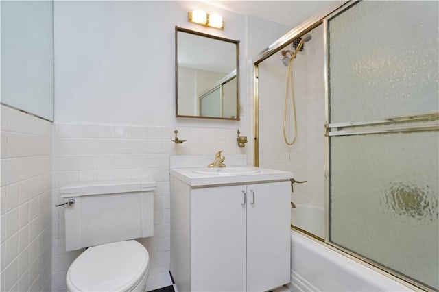 bathroom featuring tile walls, toilet, wainscoting, enclosed tub / shower combo, and vanity