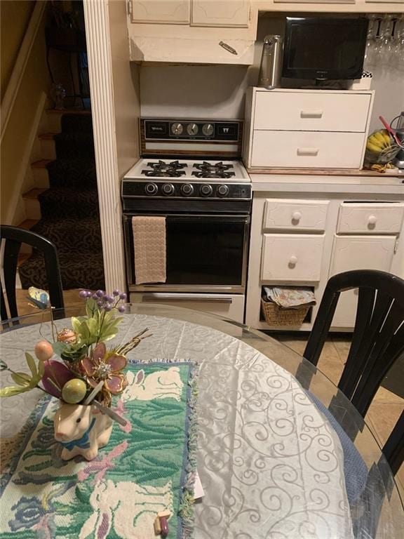 kitchen with light tile patterned flooring, white cabinetry, and gas range