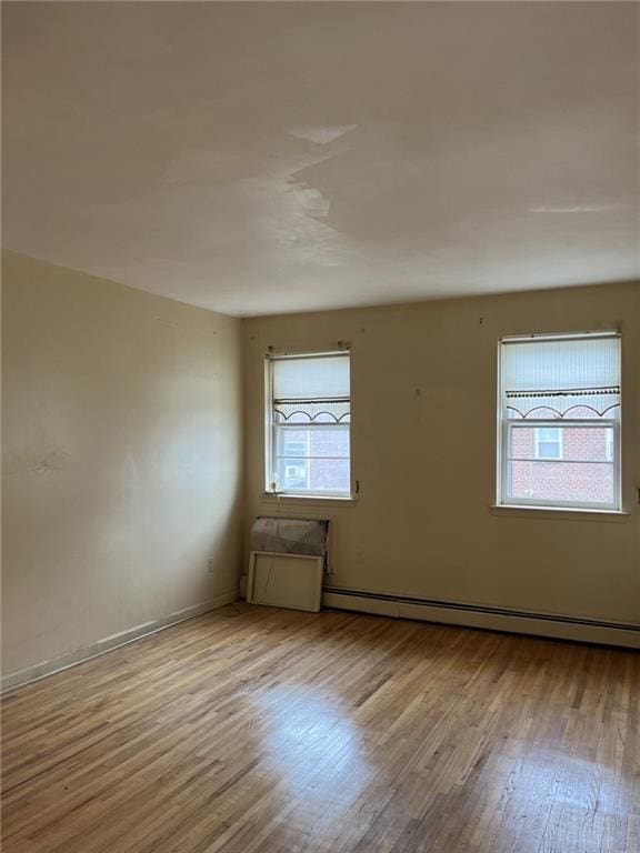 spare room featuring a baseboard heating unit and light hardwood / wood-style floors