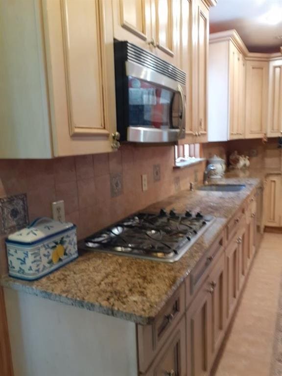 kitchen with light stone countertops, light brown cabinets, stainless steel appliances, tasteful backsplash, and sink