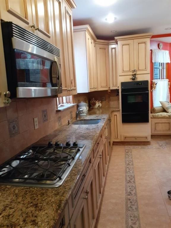 kitchen with light stone countertops, appliances with stainless steel finishes, light brown cabinetry, sink, and light tile patterned floors