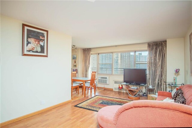 living room with a wall mounted air conditioner, radiator heating unit, and hardwood / wood-style floors