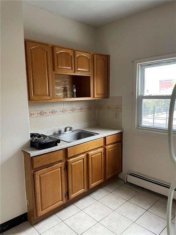 kitchen featuring light tile patterned flooring, backsplash, baseboard heating, and sink