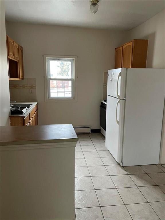 kitchen featuring stove, tasteful backsplash, baseboard heating, light tile patterned floors, and white fridge