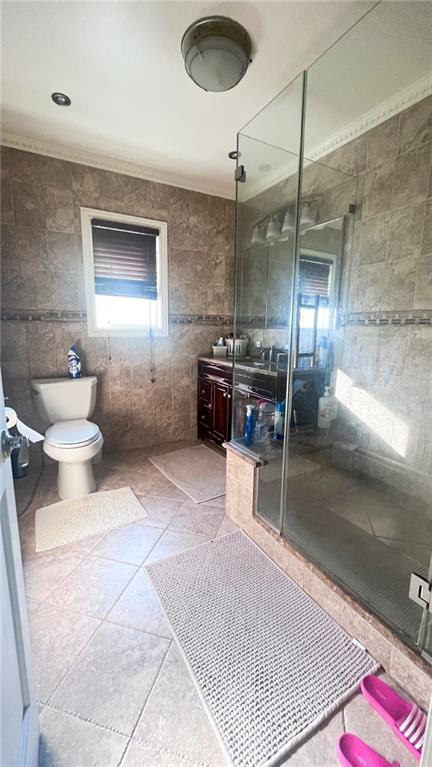 bathroom with tile walls, vanity, a shower with shower door, and toilet