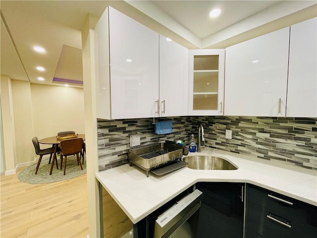 kitchen featuring decorative backsplash, dishwashing machine, light wood-style flooring, white cabinetry, and a sink