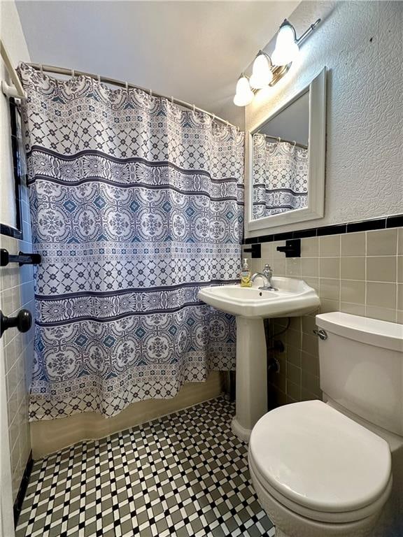 bathroom with walk in shower, toilet, and tile walls