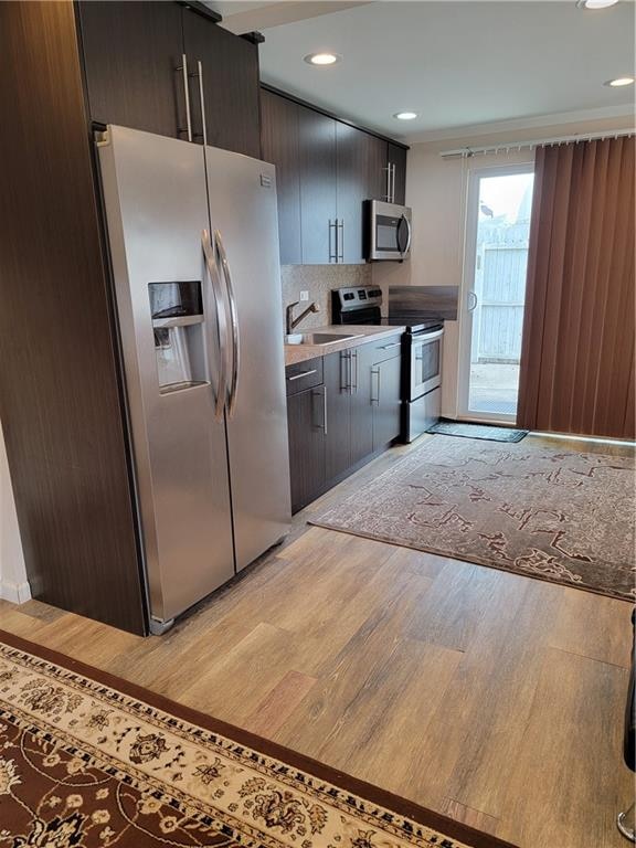 kitchen featuring appliances with stainless steel finishes, sink, decorative backsplash, dark brown cabinets, and light hardwood / wood-style flooring