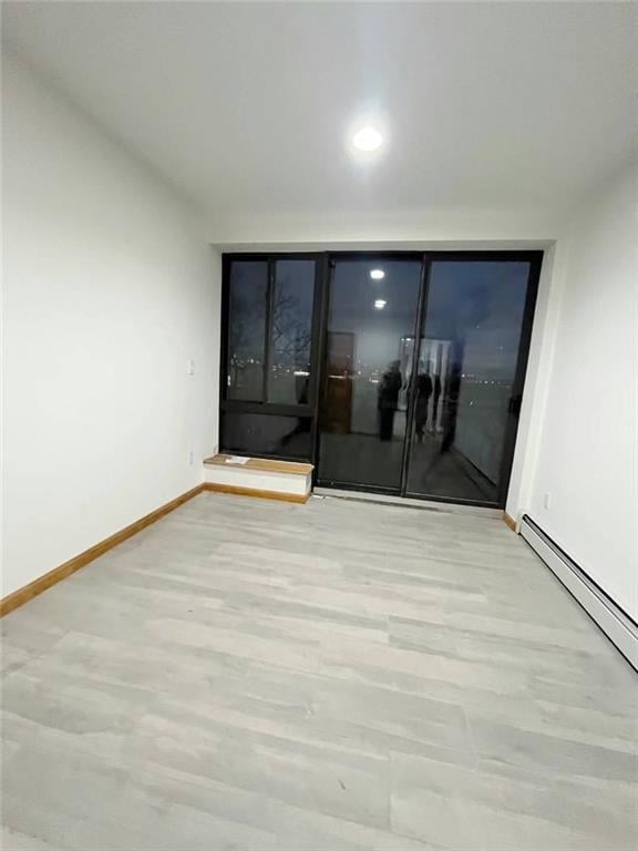 unfurnished room with a baseboard heating unit and light wood-type flooring