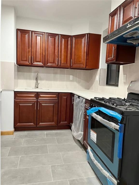 kitchen with stainless steel range with gas stovetop, sink, tasteful backsplash, and light tile flooring