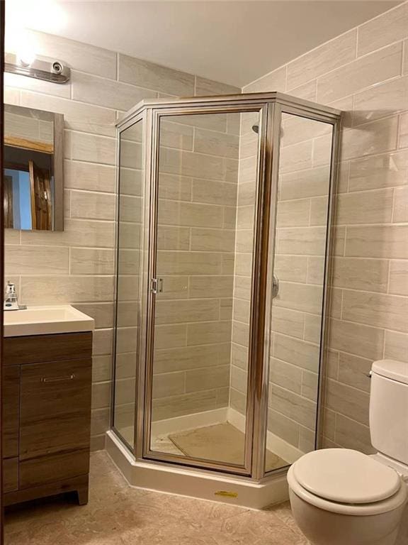 bathroom with vanity, a shower with door, tile walls, and toilet
