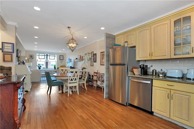 kitchen with appliances with stainless steel finishes, decorative light fixtures, backsplash, ornamental molding, and light hardwood / wood-style floors