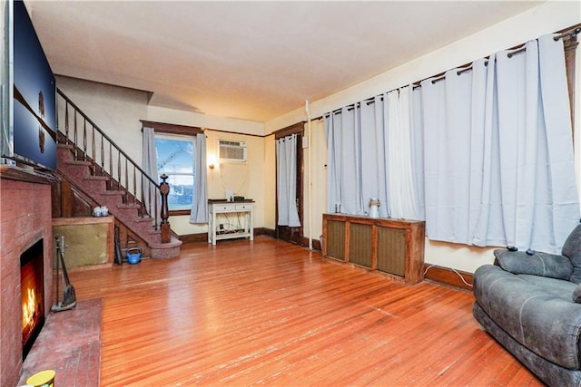 living room featuring hardwood / wood-style flooring, a brick fireplace, and an AC wall unit